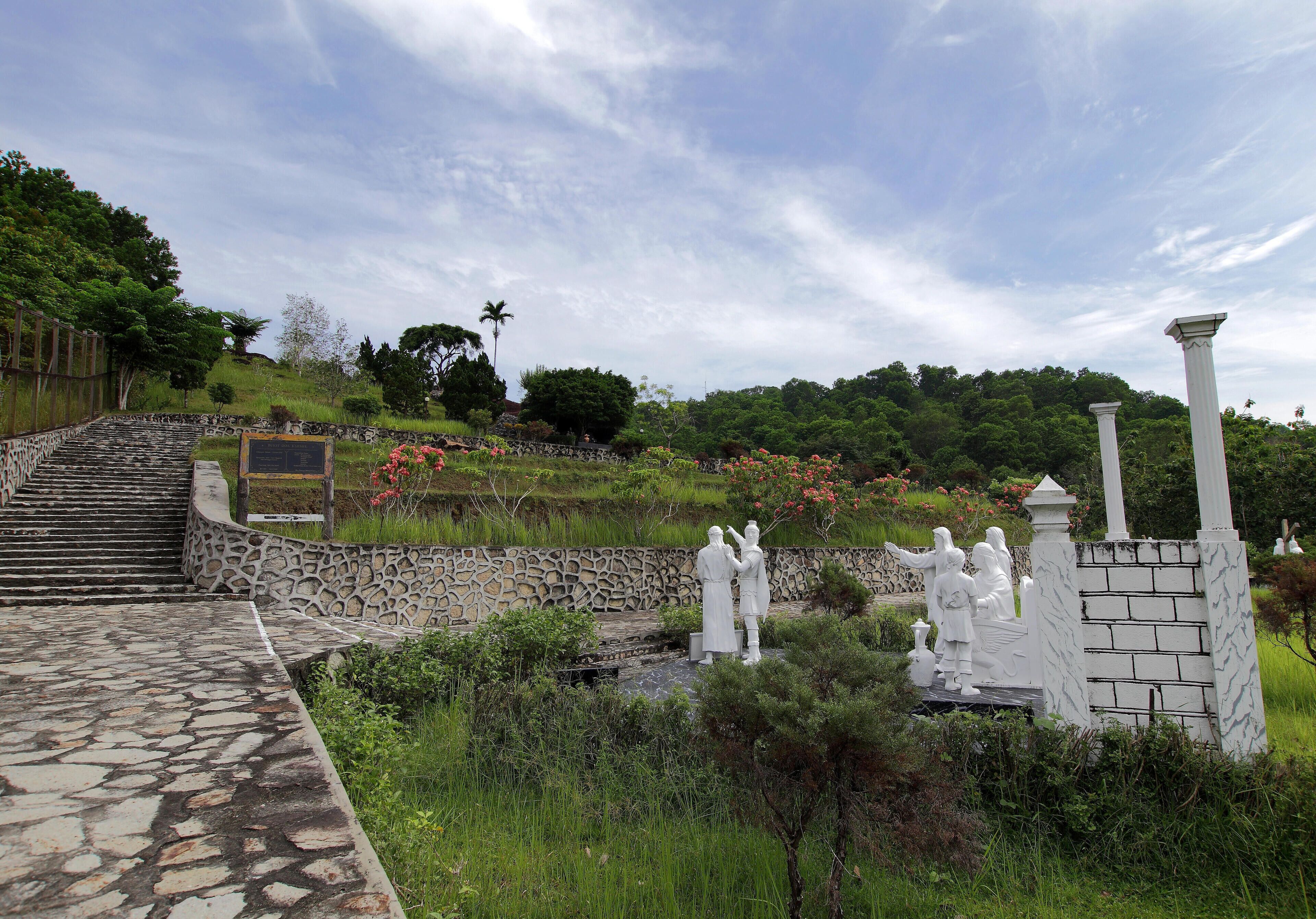 A stone pathway leading to a garden with statues and a stone wall.