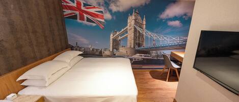 A hotel room with a large bed, a desk, a chair, and a TV. There is a mural of a bridge and a flag on the wall.