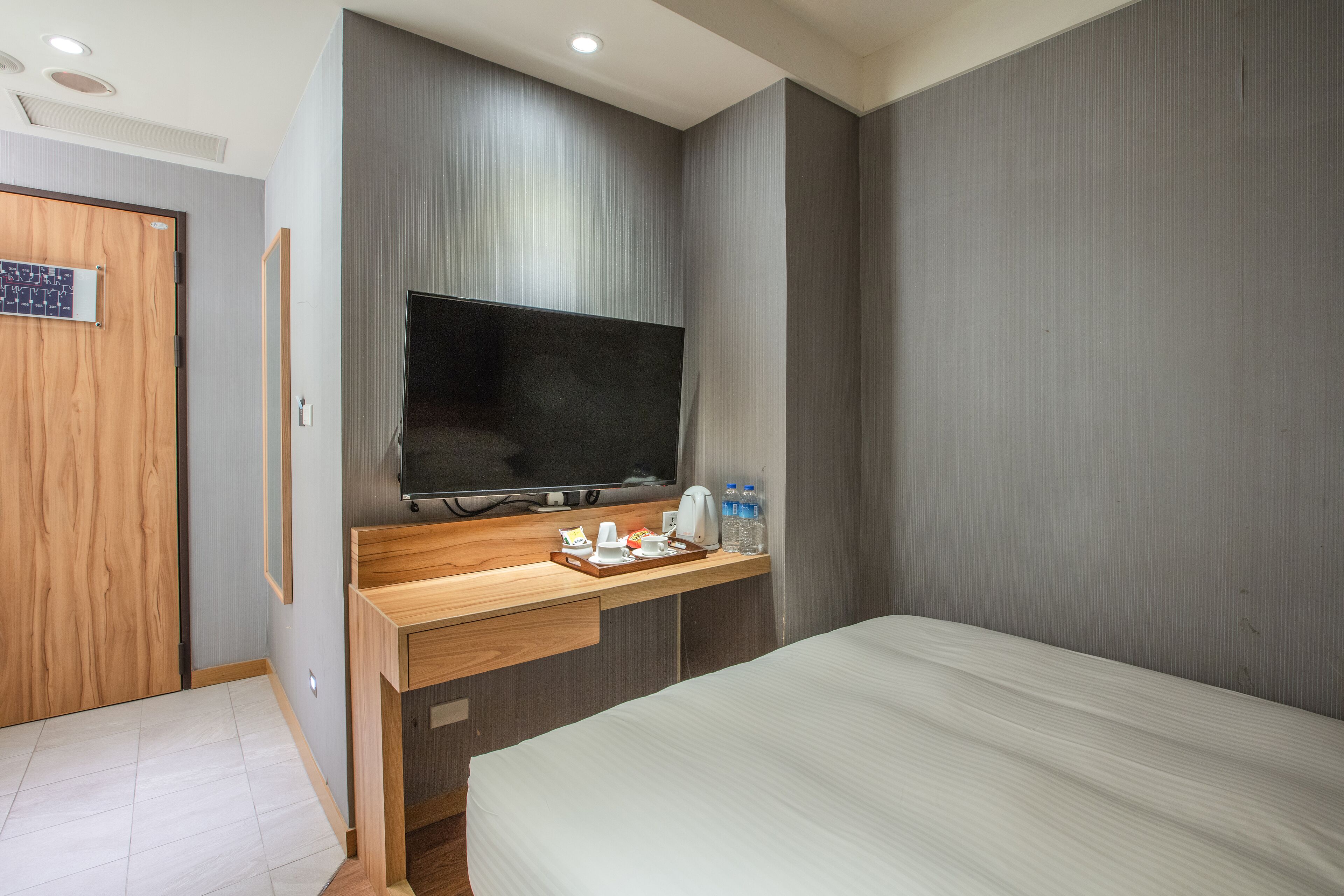 Une chambre d’hôtel moderne équipée d’un bureau en bois, d’un téléviseur à écran plat, d’un lit et d’un mini-bar.