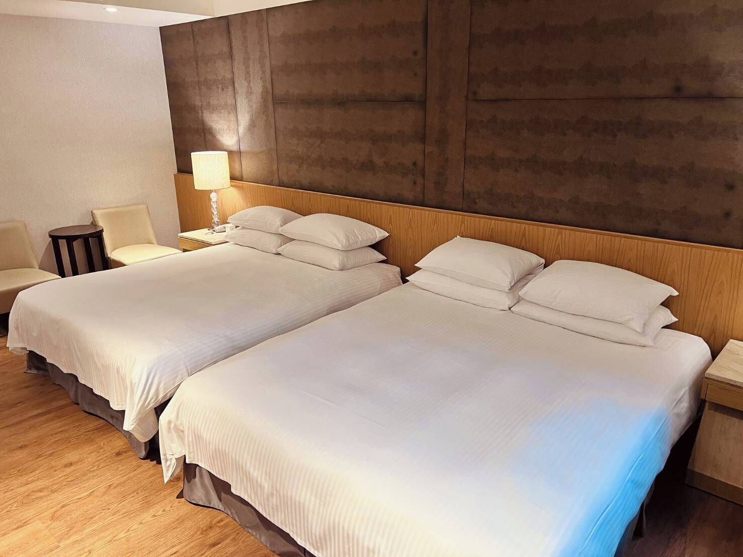 A hotel room with two beds, a chair, a nightstand, and a lamp.