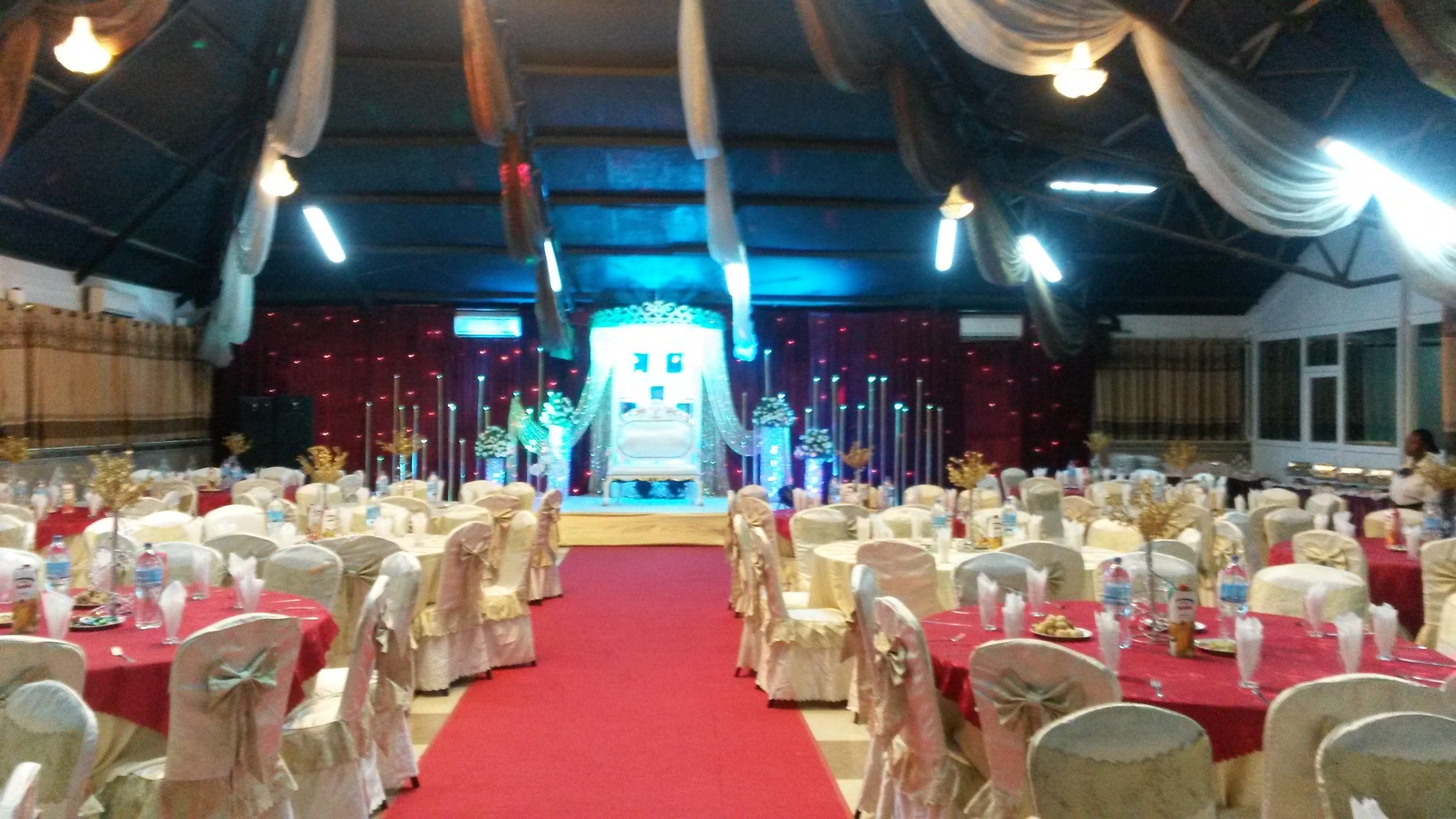 Une salle de banquet avec des tables rondes et des chaises, un tapis rouge et une scène dotée d’un fond blanc.