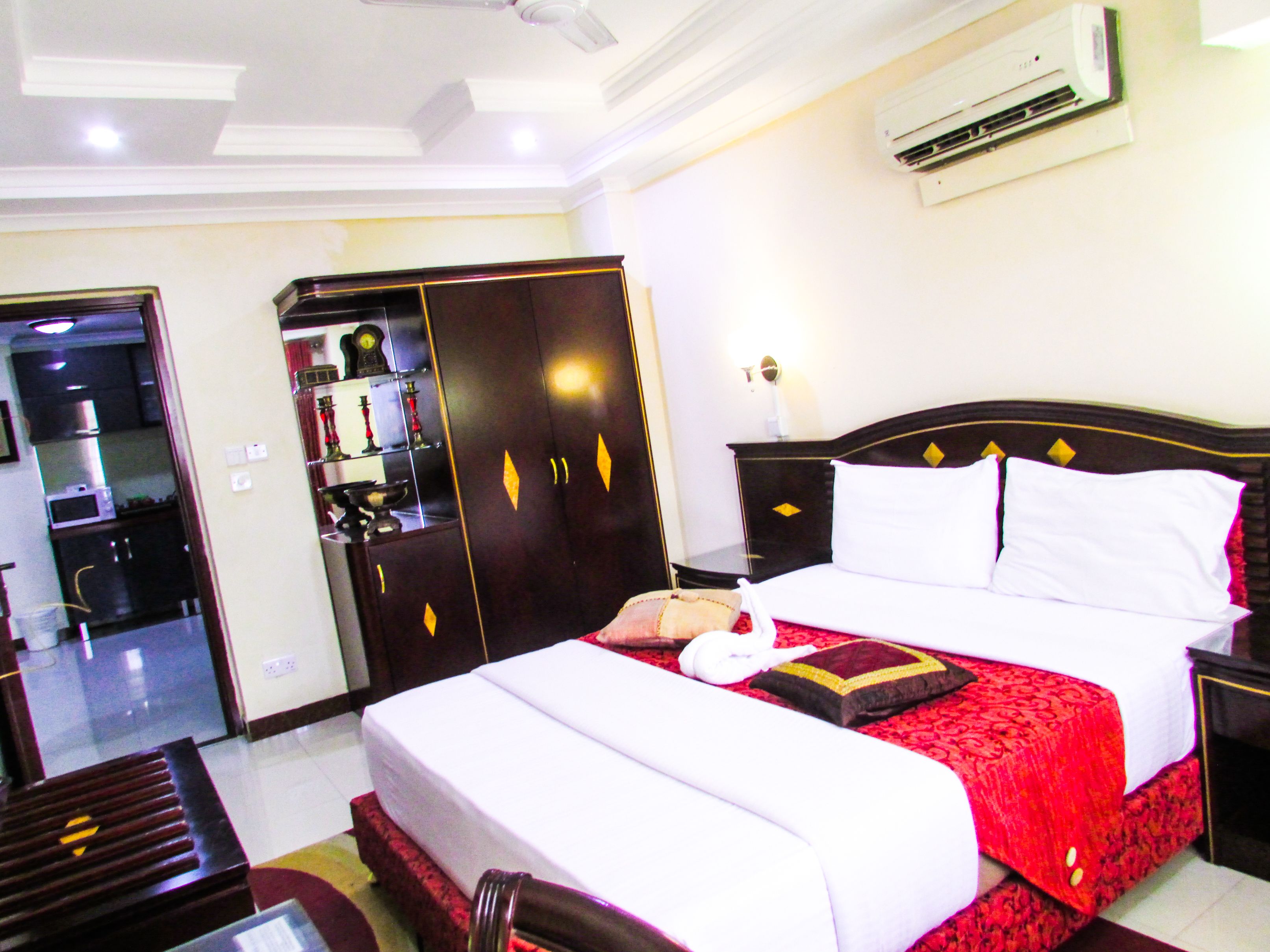 A hotel room with a bed, a wardrobe, a bedside table, and an air conditioning unit.
