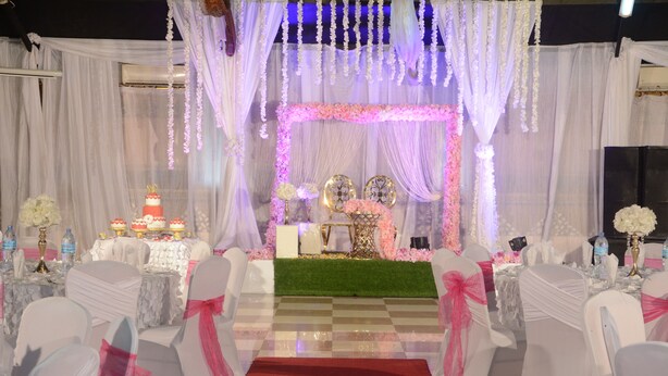 Salón para recepción de bodas con sillas blancas, alfombra roja y decoración floral.