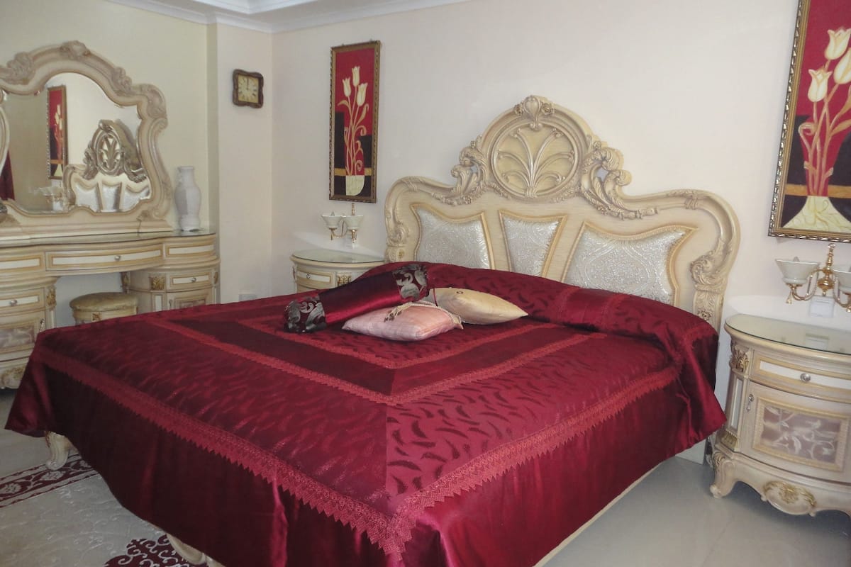 A spacious bedroom with a large bed, ornate headboard, and a classic dresser.