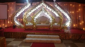 Un escenario ornamentado con un marco dorado y decoraciones florales blancas, una alfombra roja y un suelo a cuadros.