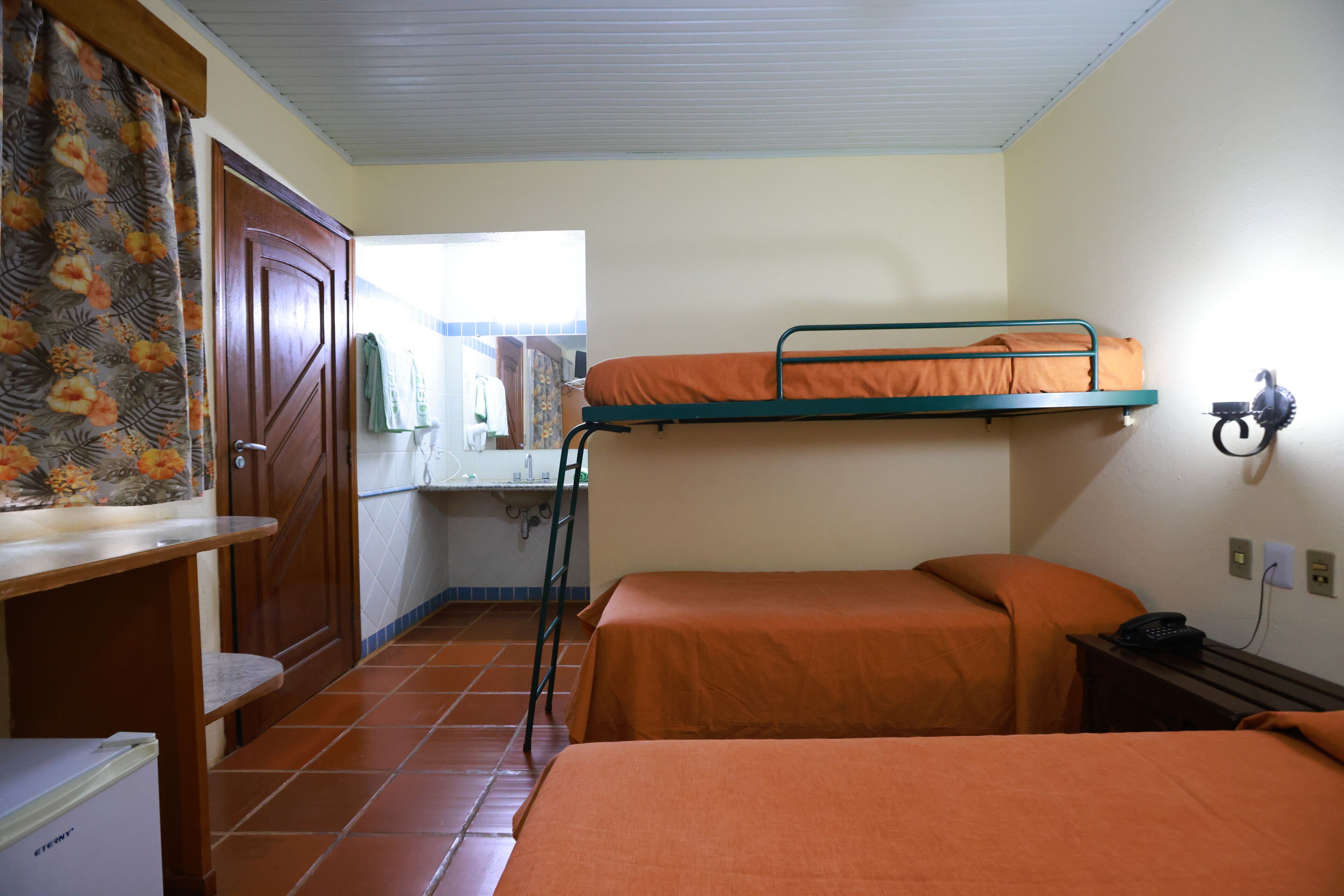 Een kamer met een stapelbed, een bureau, een stoel, een kleine koelkast en een badkamer in de achtergrond.