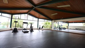 Ein geräumiger Fitnessraum mit Trainingsgeräten, großen Fenstern und einer hohen Holzbalkendecke.