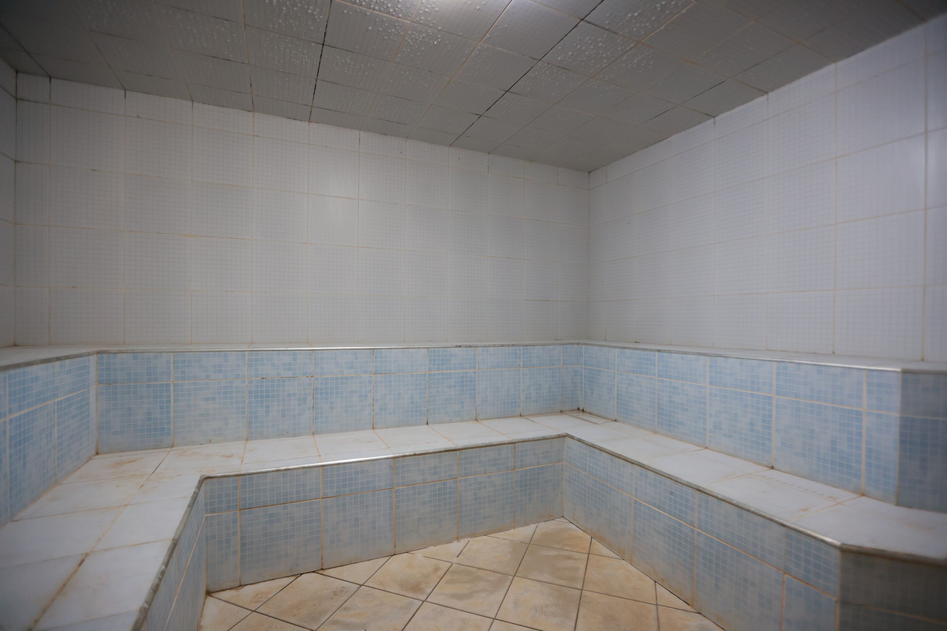 A bathroom with white and blue tiles, a corner sink, and a tiled floor.