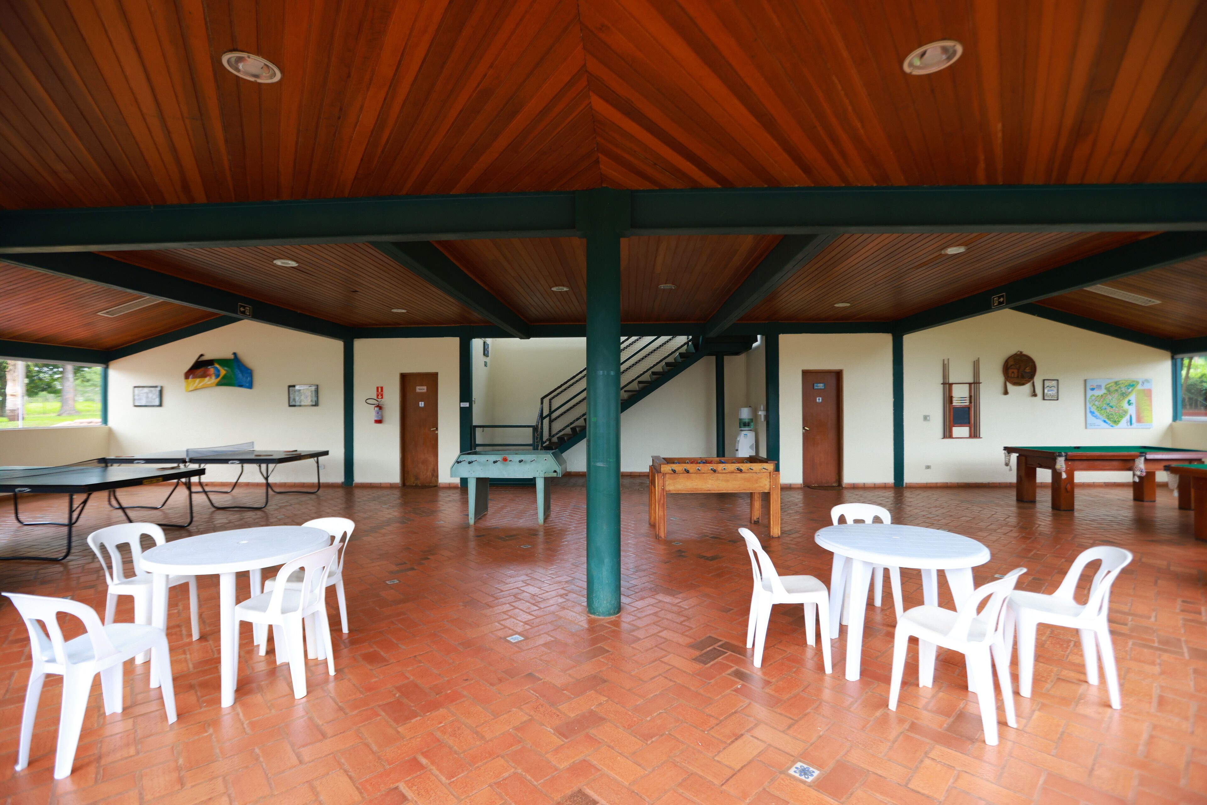 An indoor recreational area with multiple tables and chairs, a pool table, and a staircase leading to an upper level.