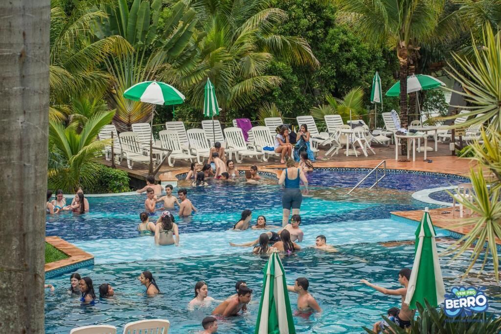 A swimming pool area with multiple lounge chairs and umbrellas, surrounded by lush greenery.