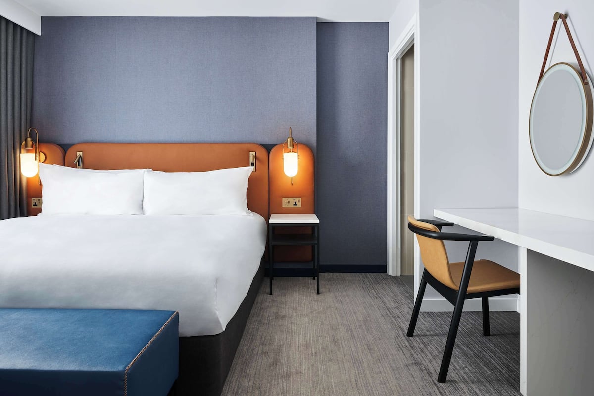 A modern hotel room with a large bed, bedside tables, a desk, and a chair.
