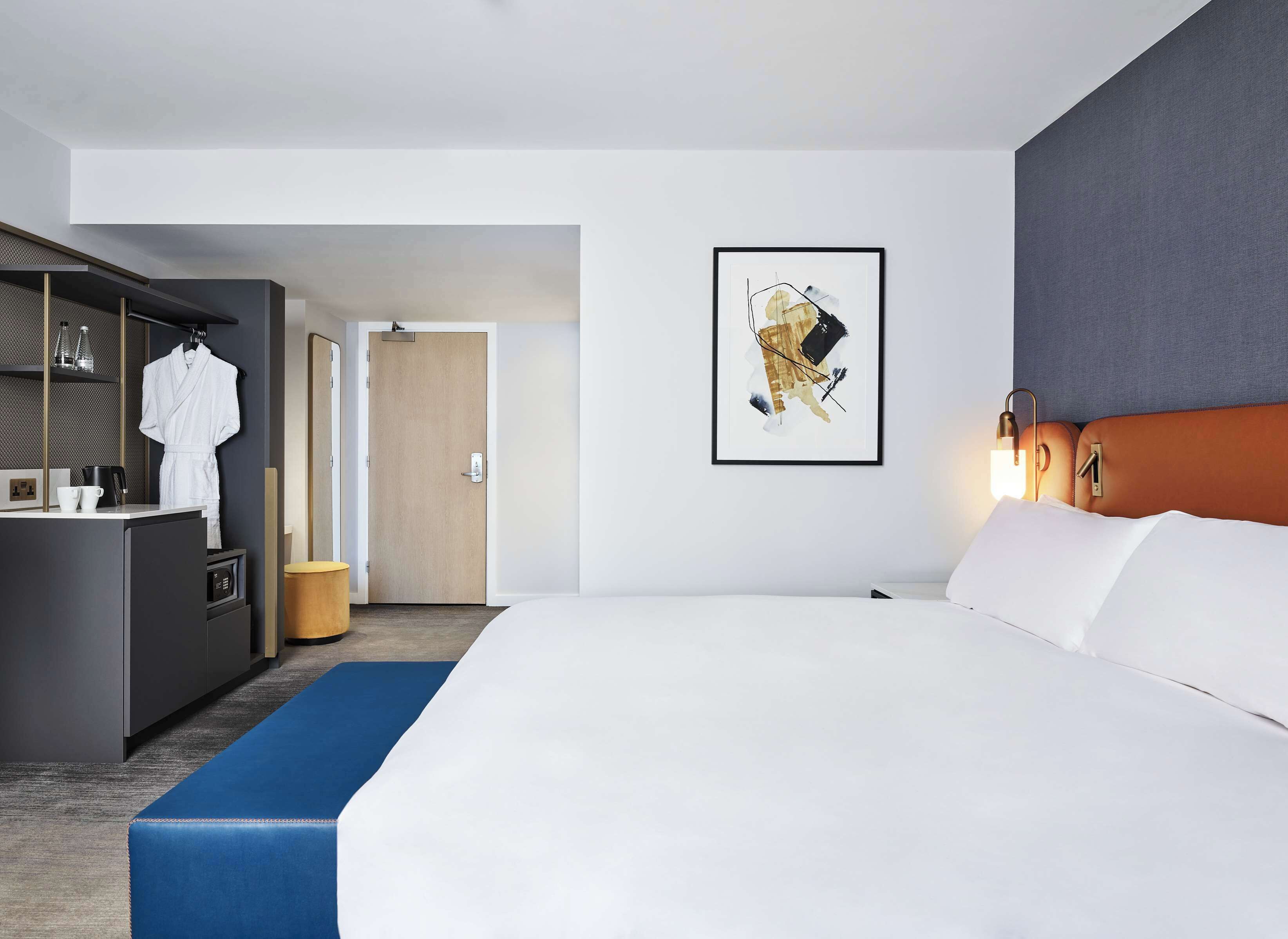 Habitación de hotel moderna con una cama grande, un escritorio con cafetera y un baño visible a través de una puerta abierta.