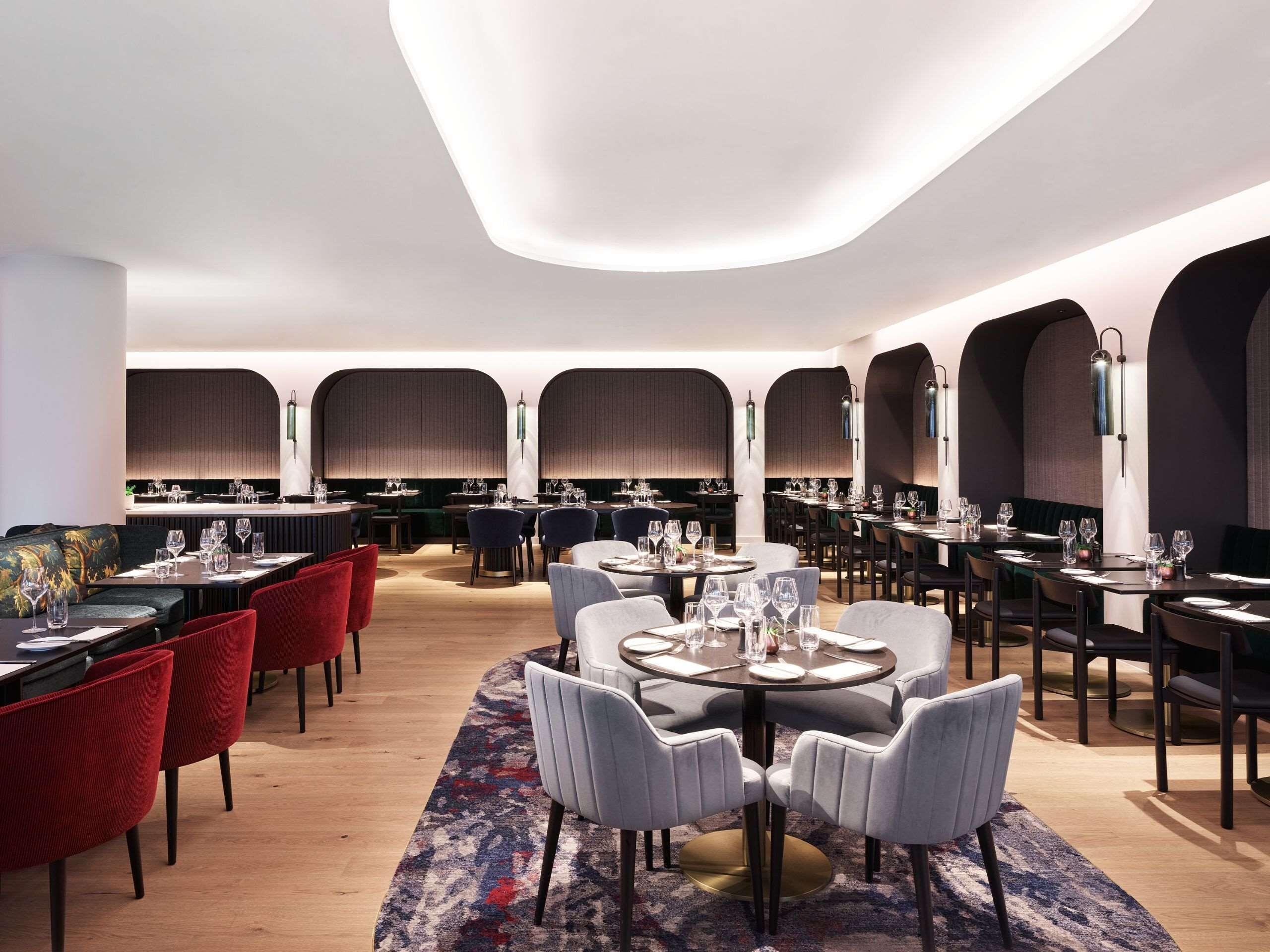 Un restaurant moderne avec des tables rondes, des chaises rouges et grises, et un espace de sièges central.