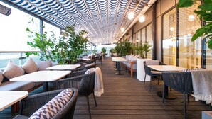 An outdoor dining area with wicker furniture and a patterned ceiling. - Hyatt Regency London Stratford (London)