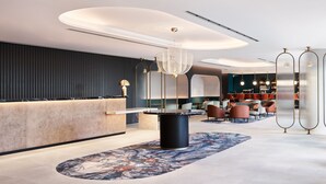 A modern hotel lobby with a reception desk, seating area, and bar. - Hyatt Regency London Stratford (London)