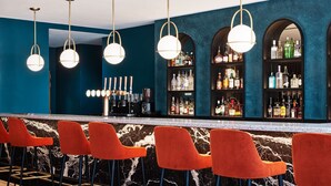 A bar area with red bar stools, a marble counter, and a blue wall with shelves of liquor bottles. - Hyatt Regency London Stratford (London)