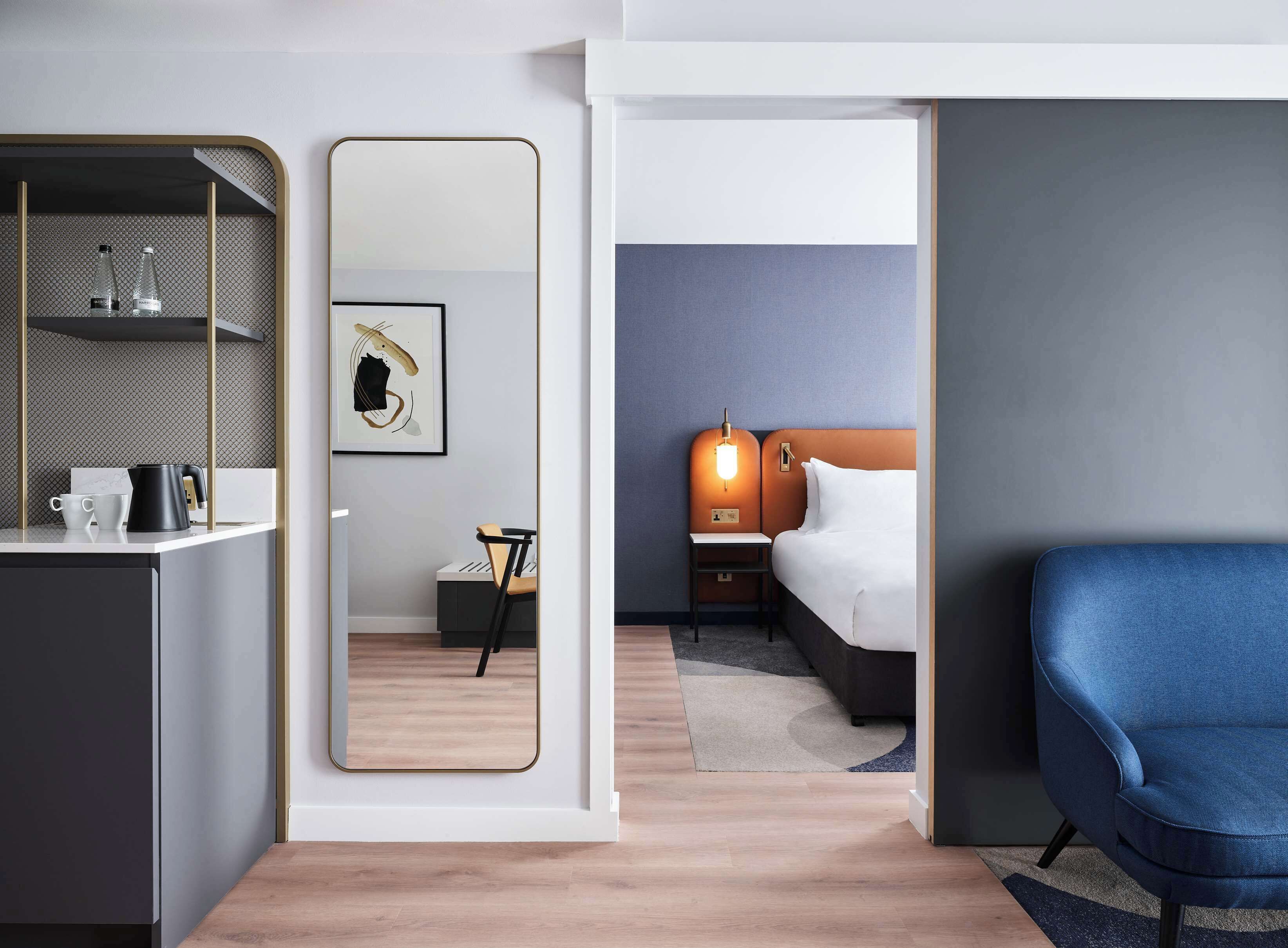 A modern hotel room with a bed, bedside table, and a blue armchair.
