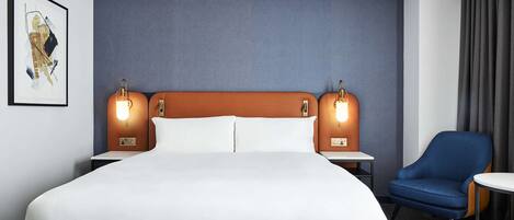 A hotel room with a large bed, two bedside tables, a chair, and a blue bench.