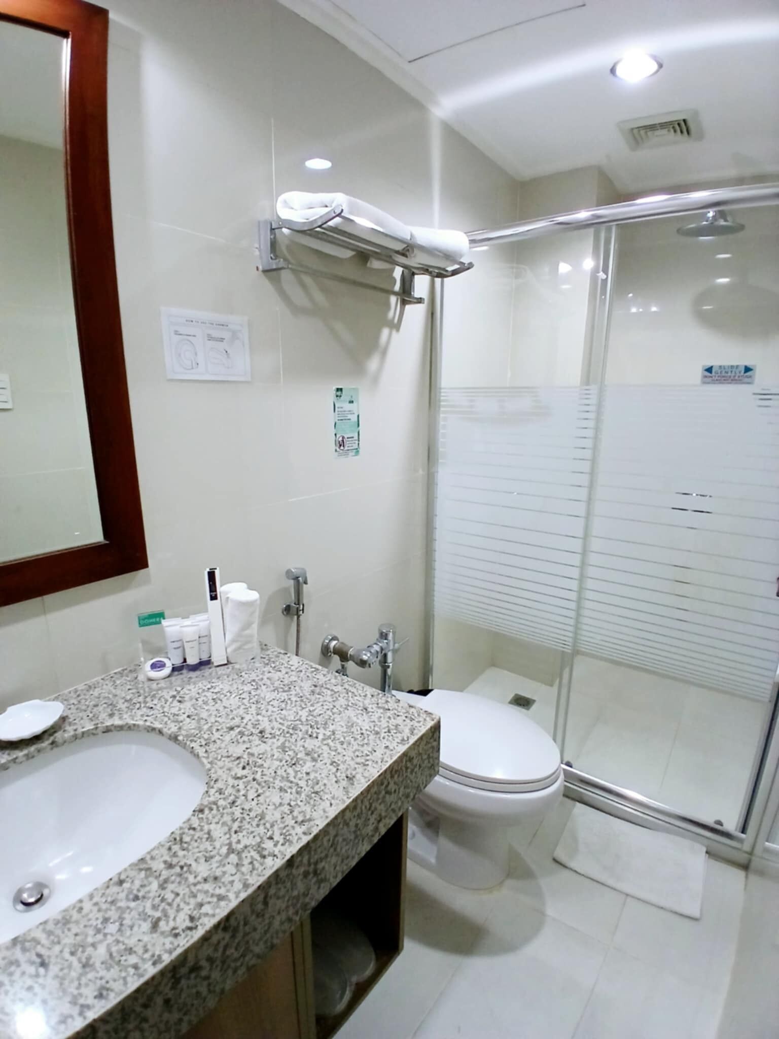 A modern bathroom with a granite countertop, a glass shower enclosure, and a white toilet.