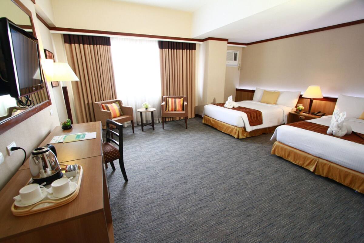 A hotel room with two beds, a desk with a coffee maker, a TV, and a small table with a plant.