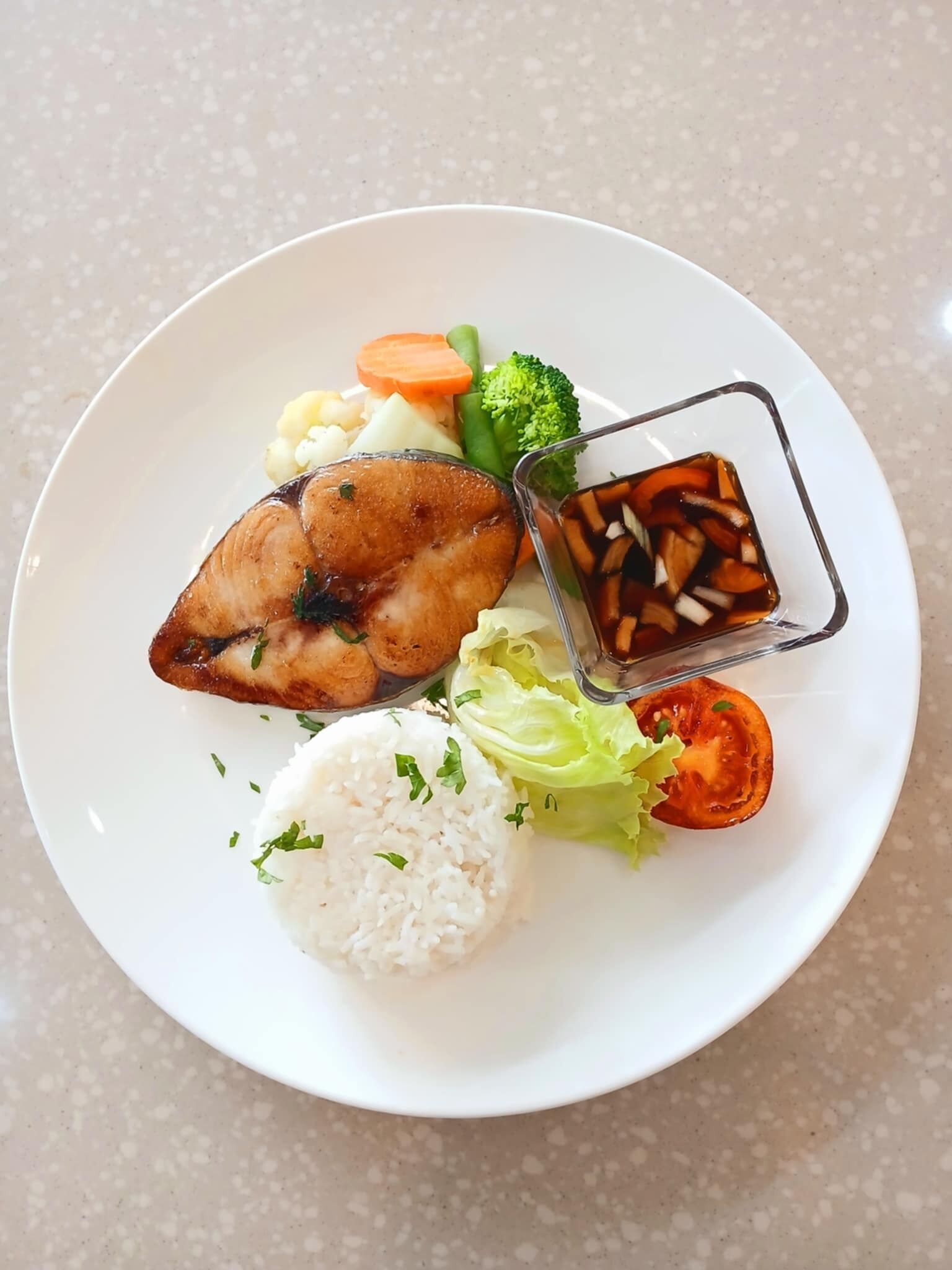 Un plato con carne a la parrilla, un recipiente pequeño de salsa, arroz y verduras.