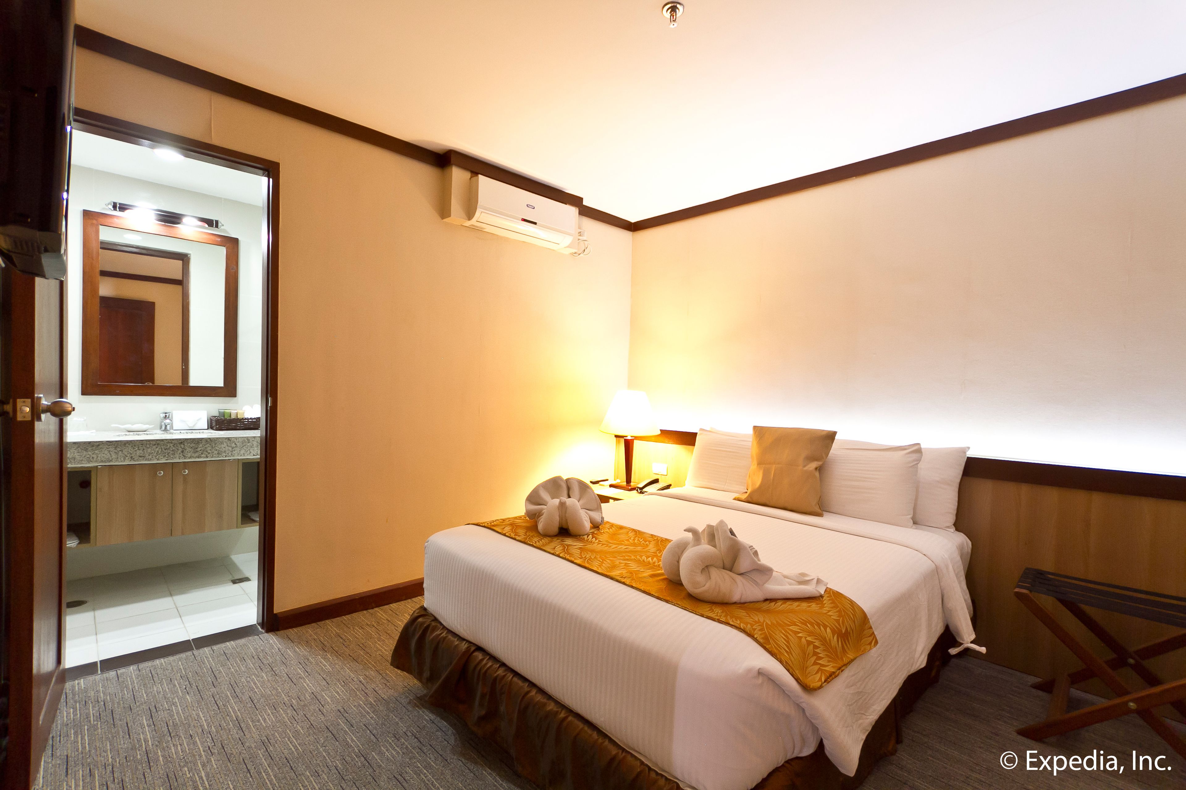 A hotel room with a bed, a bedside lamp, a mirror, and an air conditioning unit.
