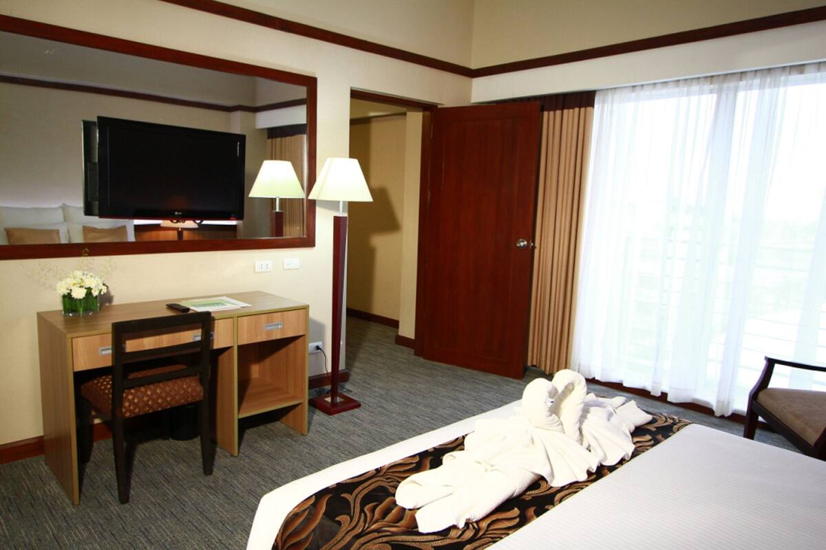 A hotel room with a bed, a desk with a chair, a television, and a door.