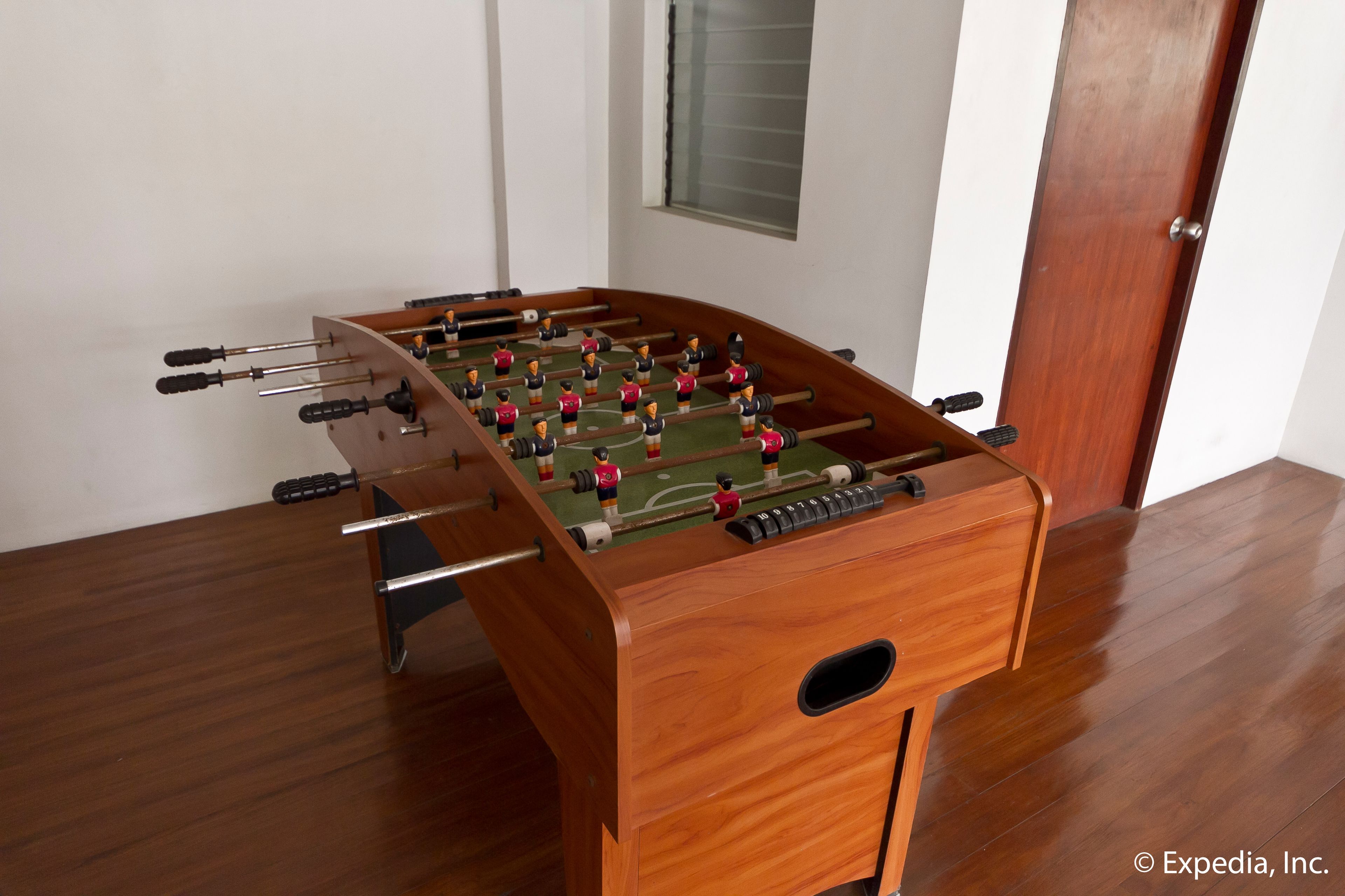 Uma mesa de futebol de madeira em um ambiente com piso de madeira e uma porta ao fundo.
