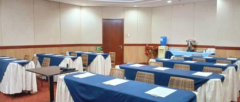 Un salón de conferencias con mesas dispuestas para reuniones, equipado con tarjetas de identificación y un dispensador de agua.