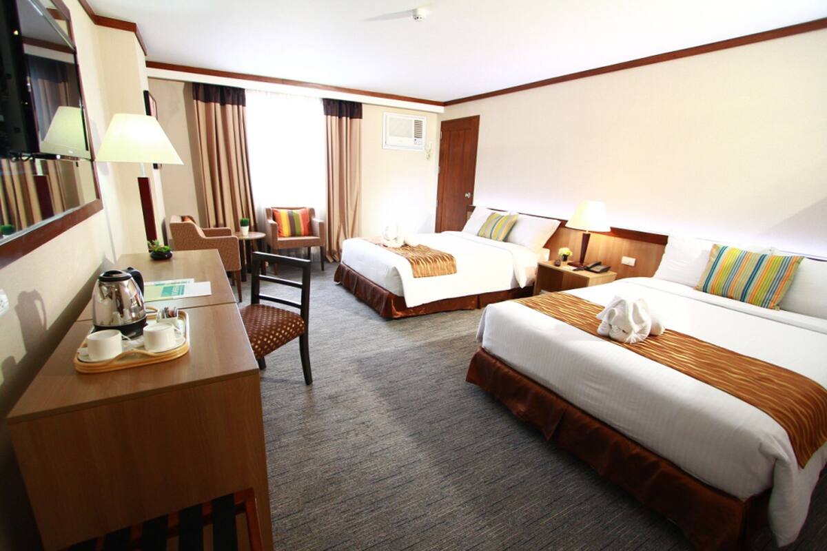 A hotel room with two beds, a desk with a coffee maker, a chair, and a small table.
