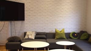 Een moderne woonkamer met een grijze bank, twee witte ronde tafels en een flatscreen televisie die aan een witte baksteenmuur is bevestigd.