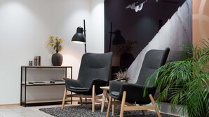 Een moderne woonkamer met twee grijze fauteuils, een zwarte vloerlamp, een boekenkast en een groot muurschilderij.