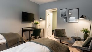 Een moderne hotelkamer met een bed, twee stoelen, een bureau, een televisie en kunstwerken in lijsten aan de muur.