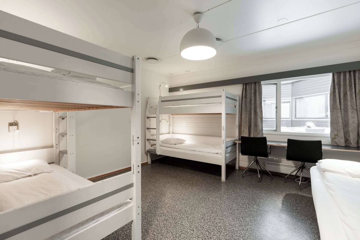 Une chambre avec un lit superposé, un bureau et des chaises, une fenêtre avec des rideaux et un luminaire au plafond.