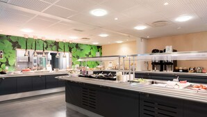 Een moderne keuken met roestvrijstalen apparatuur, een wand met groene bladeren en een buffetopstelling.