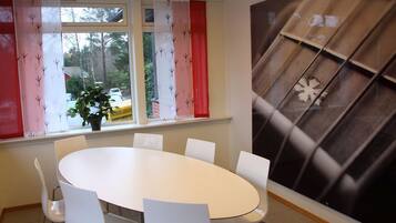 A dining area with a round table and white chairs, a window with curtains, and a wall with a geometric pattern.