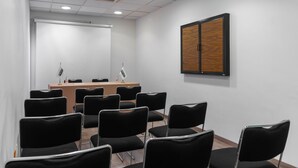 Un salón de conferencias con una larga mesa, sillas negras, una pizarra y un panel de madera en la pared.