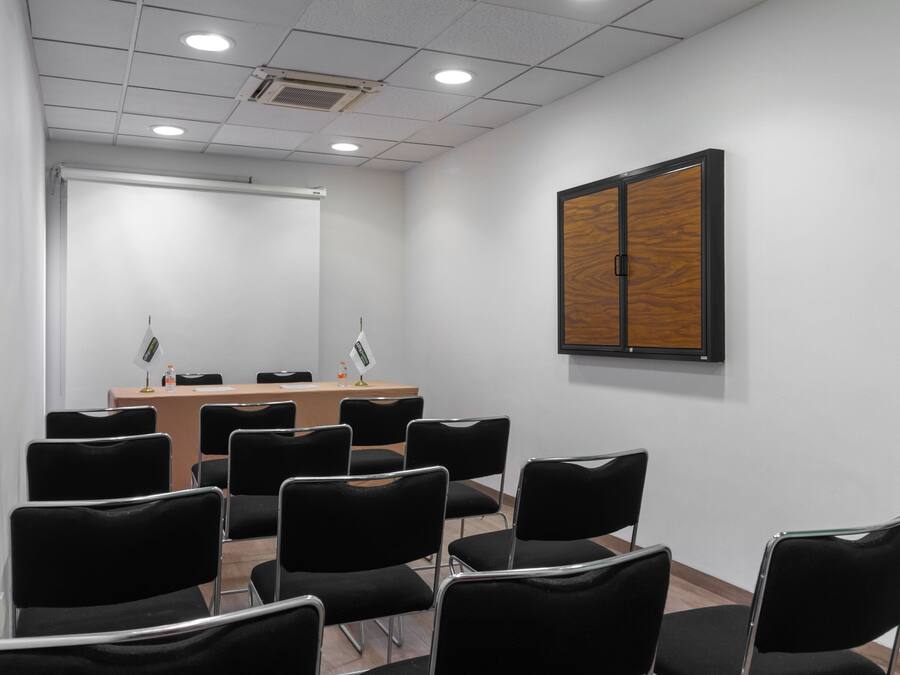 Uma sala de conferências com uma mesa comprida, cadeiras pretas, um quadro branco e um painel de madeira na parede.