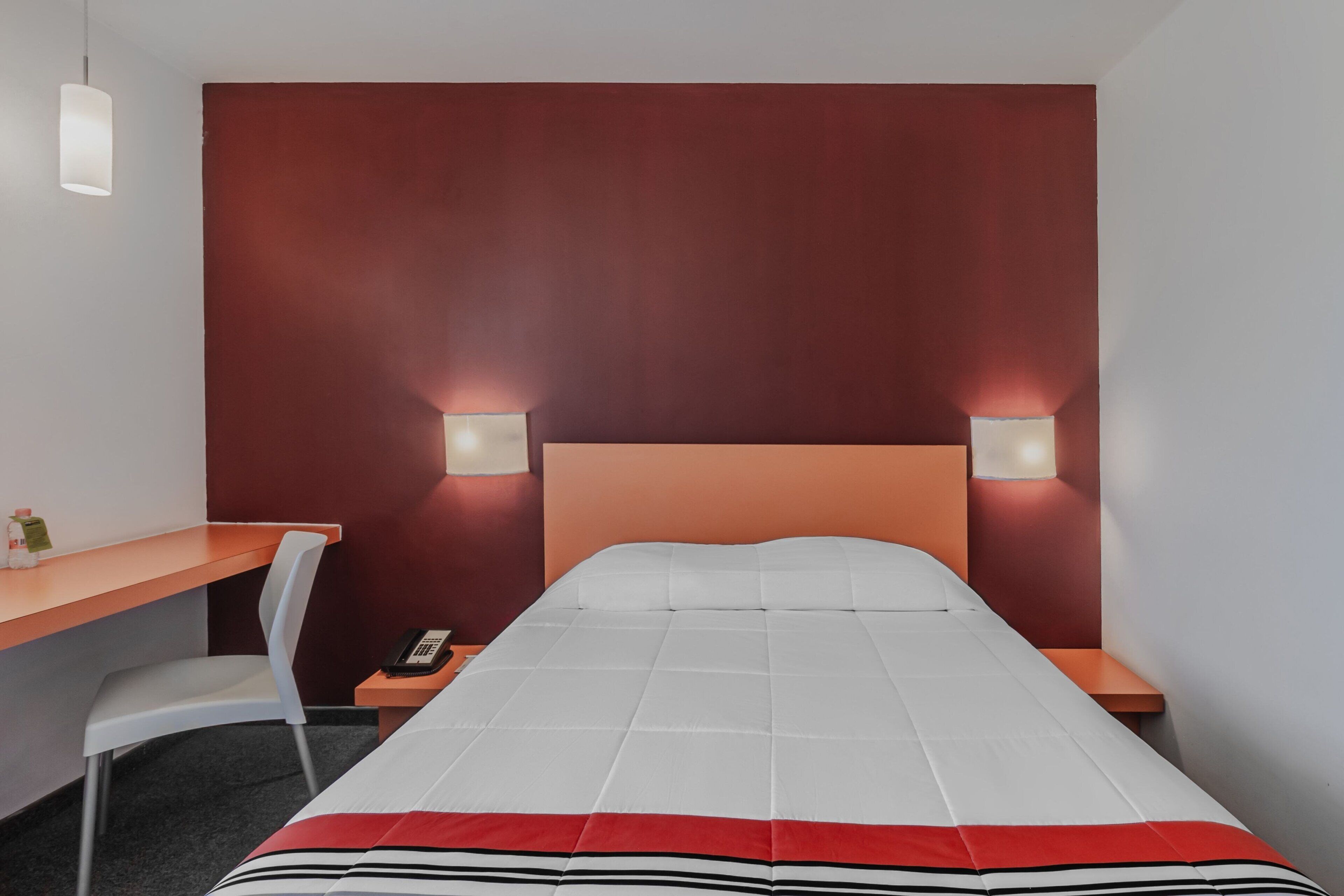 A hotel room with a bed, a desk, a chair, and two bedside lamps.