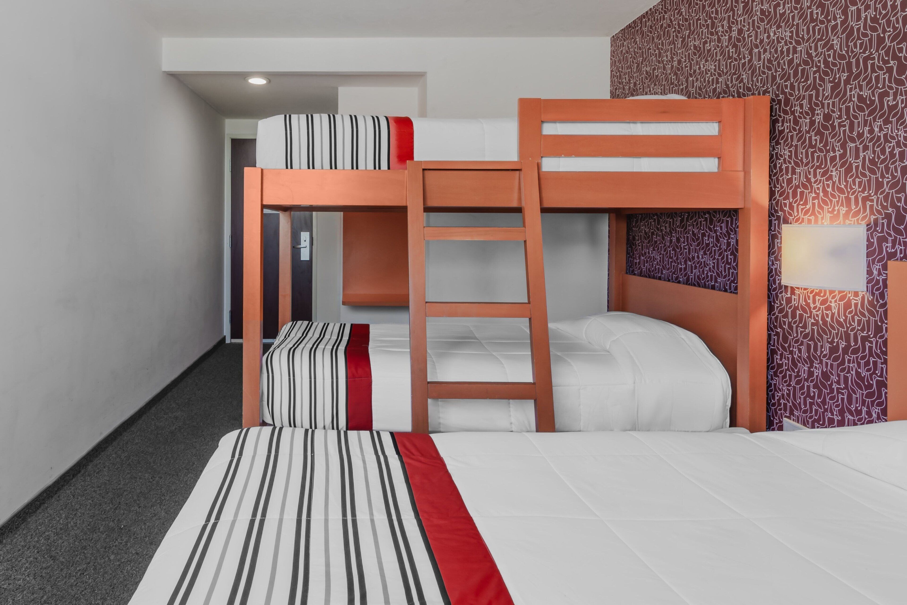 Habitación con literas, una colcha a rayas, una escalera de madera y un papel tapiz estampado.