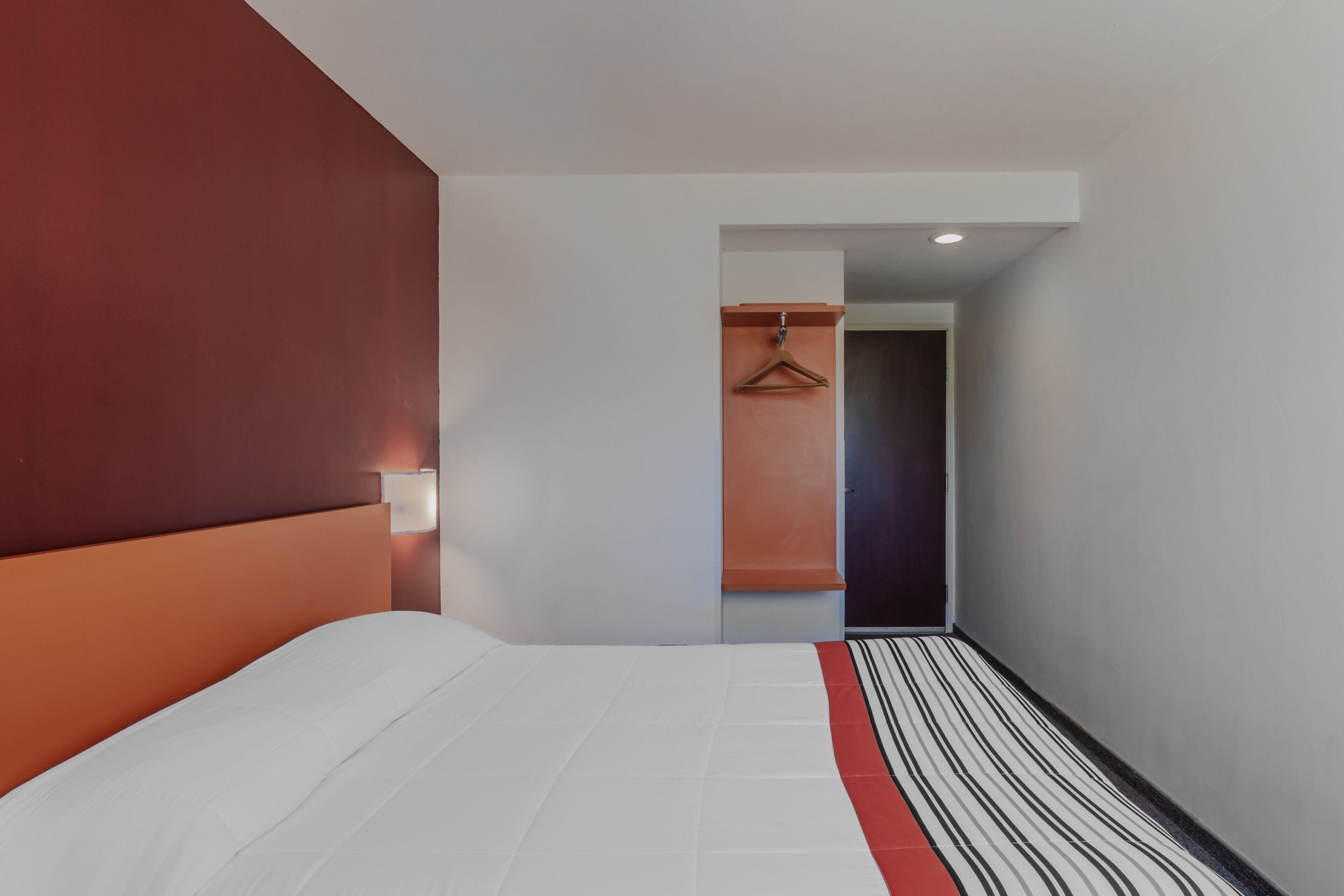 Una habitación de hotel con una cama, un cabecero rojo, un tapete a rayas y un perchero.