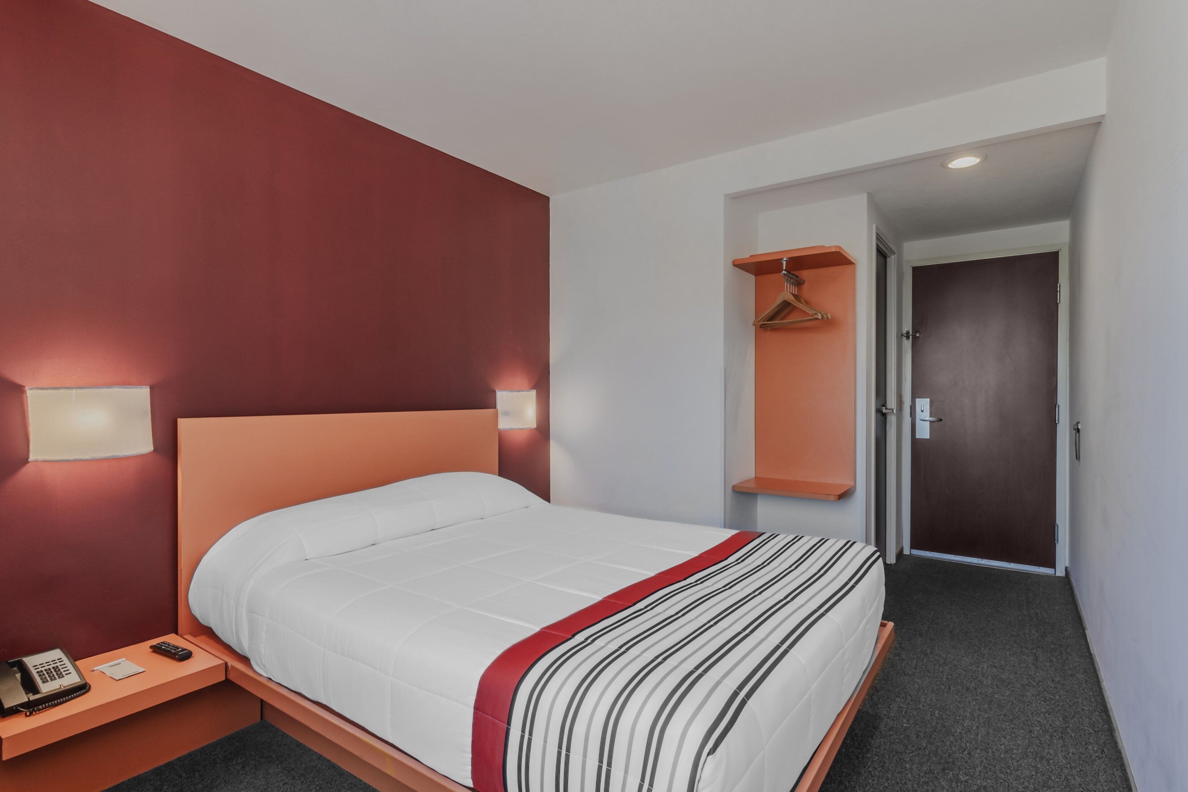 A hotel room with a bed, bedside table, lamp, and a door leading to another room.