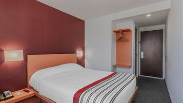 A hotel room with a bed, bedside table, lamp, and a door leading to another room.