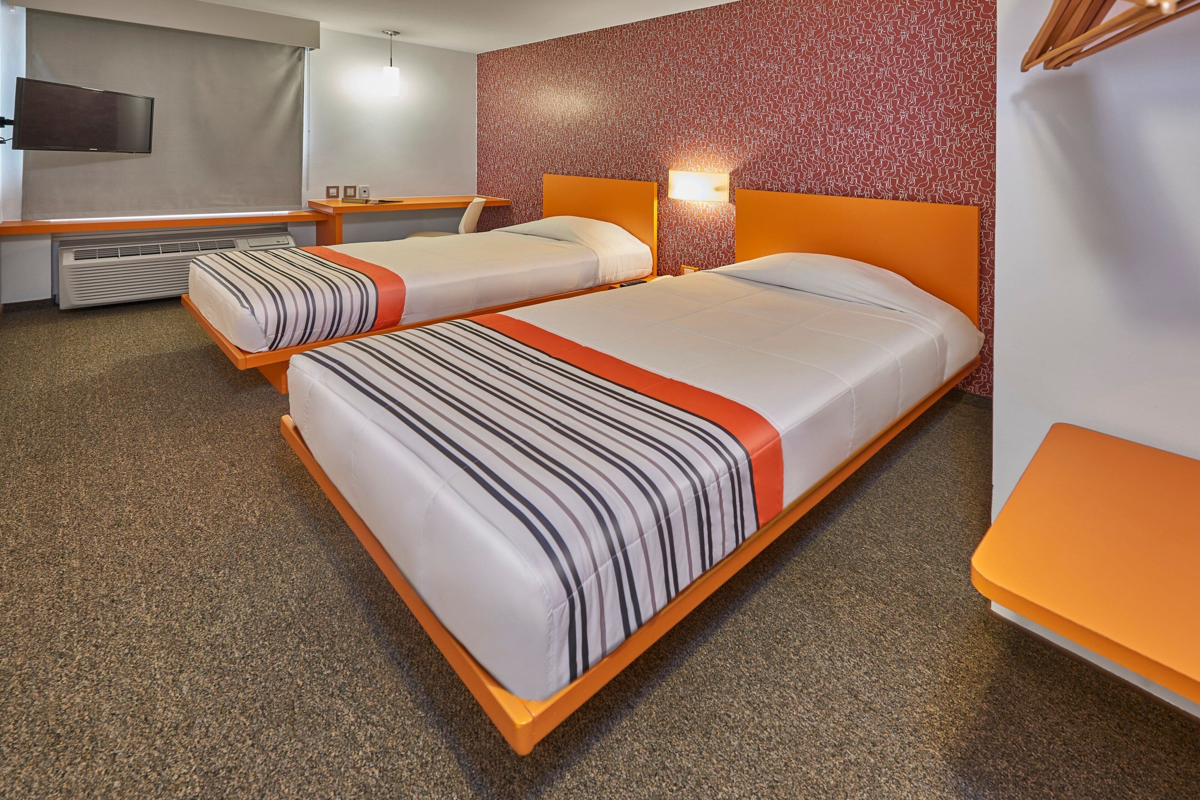 A hotel room with two beds, a TV, a heater, and a patterned wall.