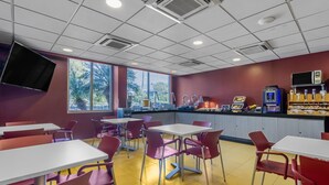 Una cafetería con mesas y sillas, una barra con alimentos y una máquina expendedora.