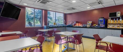 A cafeteria with tables and chairs, a counter with food items, and a vending machine.