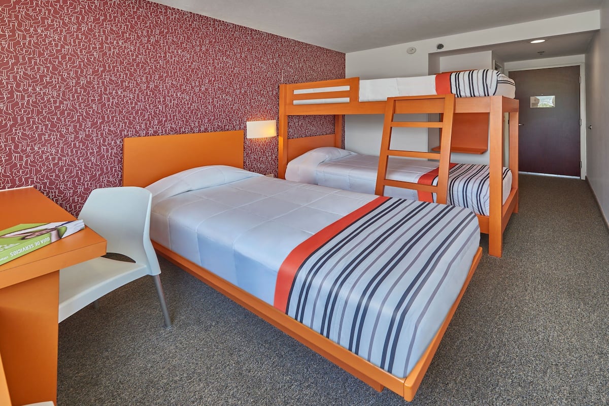 Une chambre d’hôtel avec des lits superposés, un bureau avec une chaise et un mur décoré de motifs.
