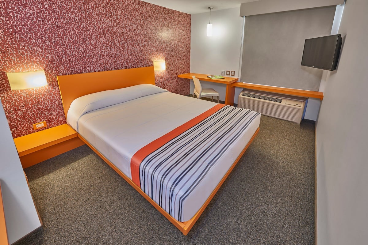 Une chambre d’hôtel équipée d’un lit, d’un bureau, d’une chaise, d’une télévision et d’un radiateur fixé au mur.
