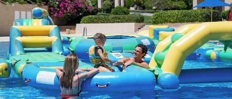 A pool area with inflatable water toys and a building with arches in the background.