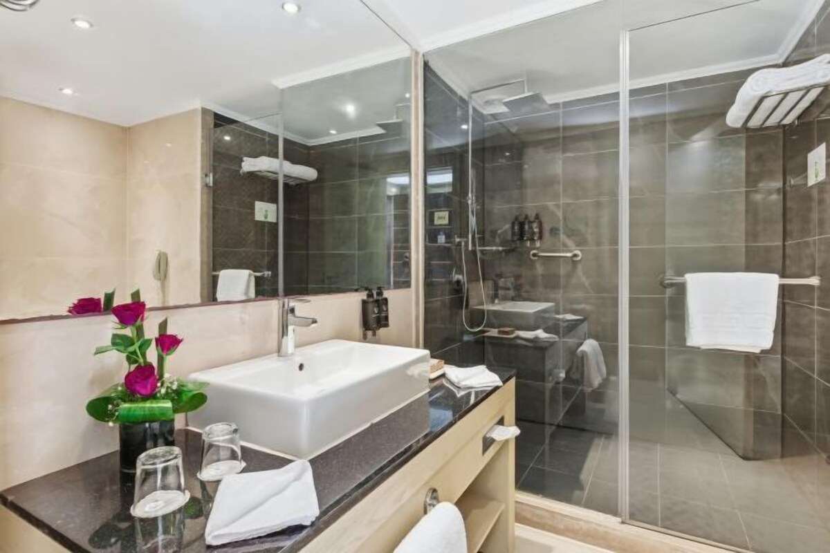 Un baño moderno con ducha envuelta en vidrio, un lavamanos espacioso y un tocador con espejo.